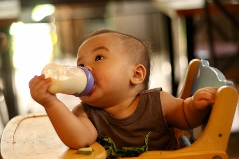 Cute baby in a high chair drinking milk from a bottle indoors, showcasing innocence and nourishment.
